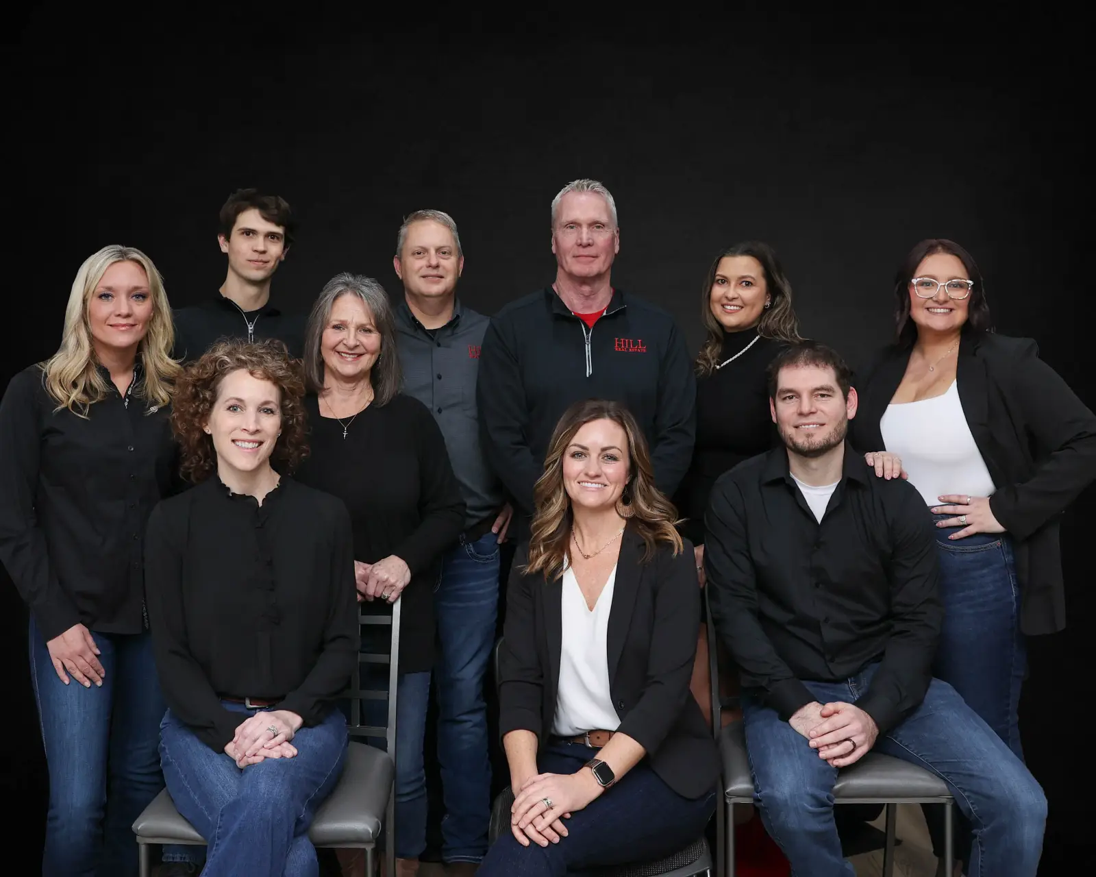 The Hill Real Estate team of ten agents posed together in front of a black backdrop